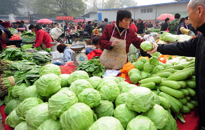 北京农贸市场在减少 man buying vegetables from a woman at a beijing farmer's market