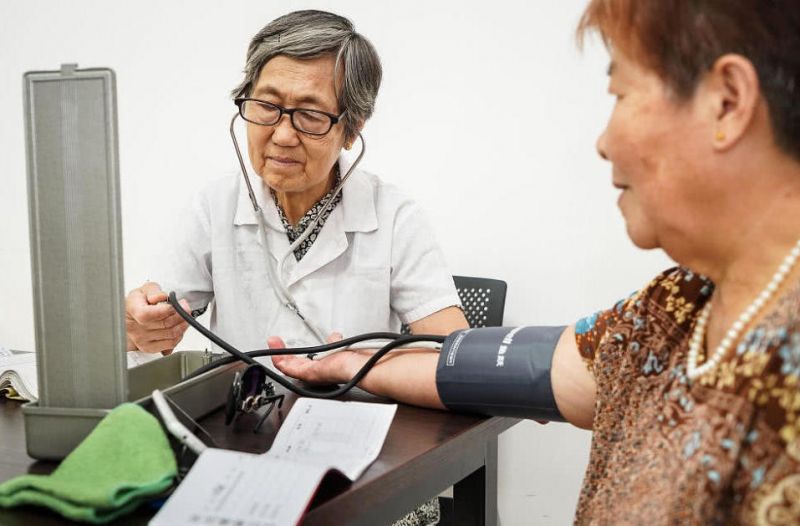 80岁老人免费给病人看病 elderly doctor taking patient's blood pressure in china