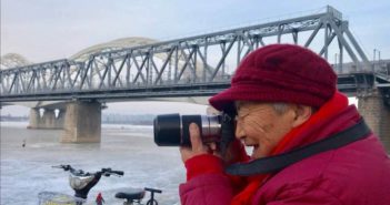 哈尔滨93岁老人59年拍了七万多张照片 side view of elderly woman taking photo next to a river