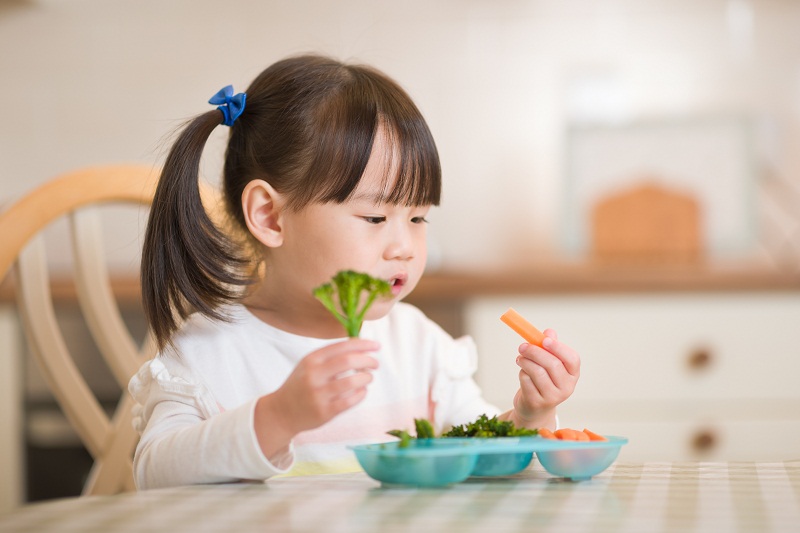 young asian girl eating vegetables at table